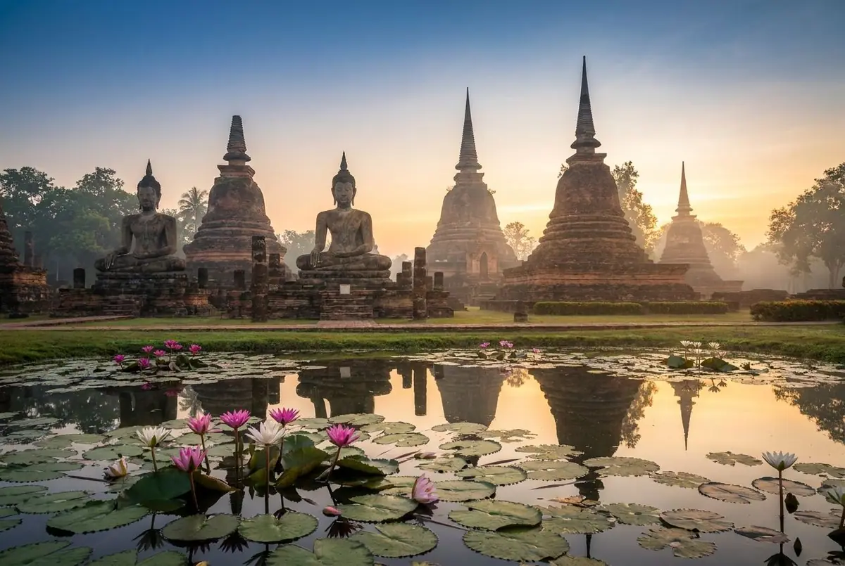 Seated Buddha statues and a lotus-bud chedi at Wat Mahathat in Sukhothai Historical Park at dawn, lotus pond in front